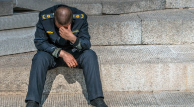 Sad policeman is sitting on the floor with his had down, he lost his job, he is alone.