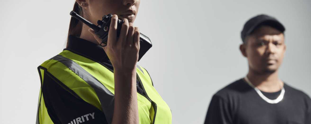 Female security guard communicating via walkie-talkie while monitoring a situation, highlighting guard duties.
