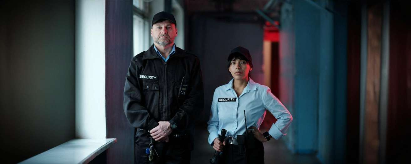 Two security officers standing confidently in a dimly lit corridor. Security jobs at National ASB Conference & Awards 2025