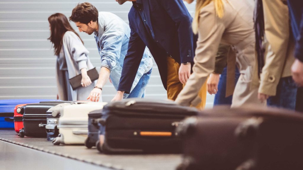 Passengers at airport baggage claim, helping to protect against luggage theft.