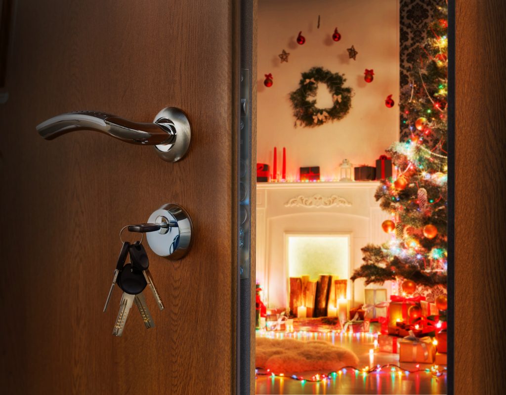 Opening door to decorated holiday interior with fireplace, garland lights and christmas tree.