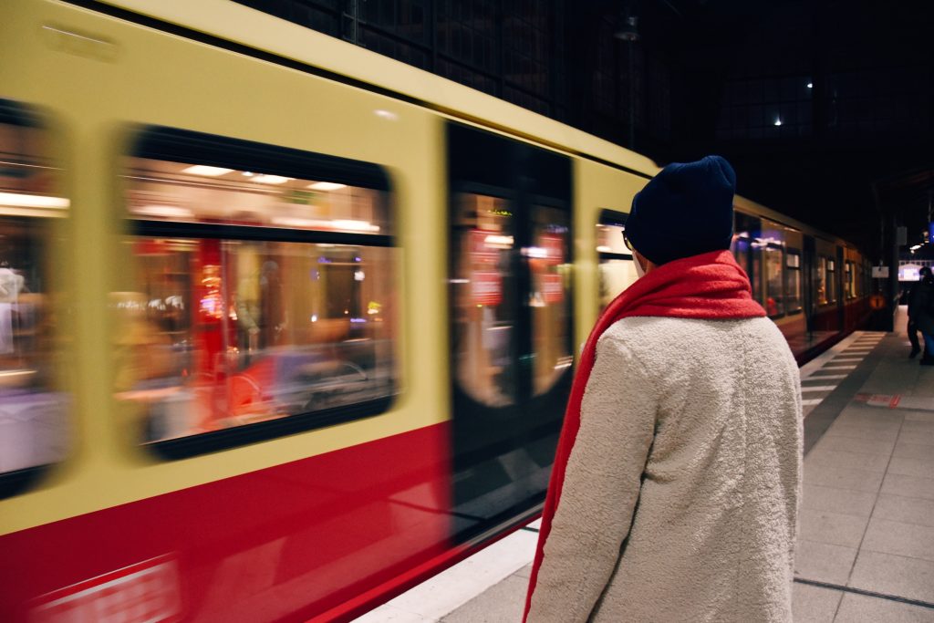 Person dressed in winter clothing watching trains pass in a UK railway station.